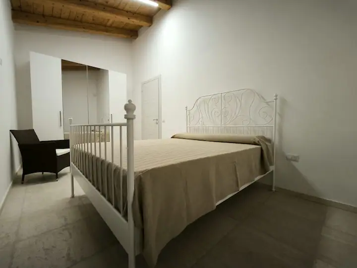 Camera matrimoniale con letto in ferro battuto bianco, poltrona e armadio a muro