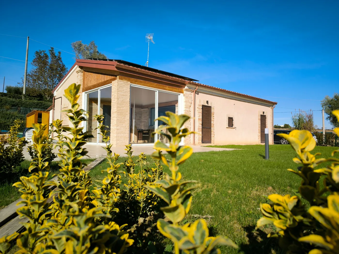 La villa a un piano con la veranda vetrata, il prato e le siepi in una giornata di sole