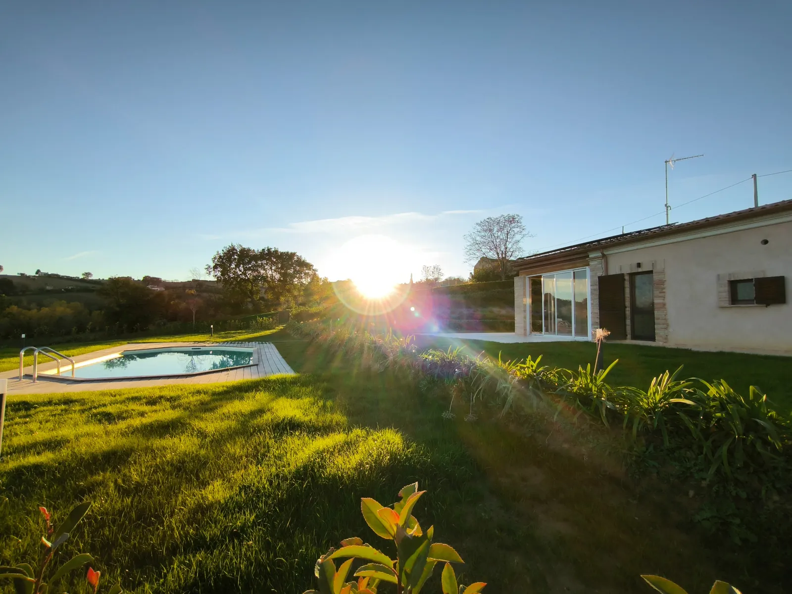 Il sole che tramonta dietro gli alberi, tra la piscina e la villa